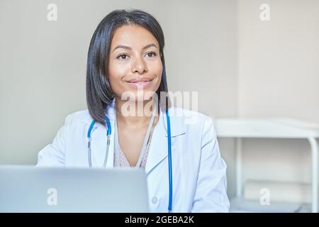 Sorridente afro medico americano femmina con stetoscopio sulle spalle in attesa di cliente in ospedale Foto Stock