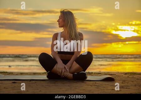 Yoga durante il tramonto a riva da donna su tappetino. Foto Stock