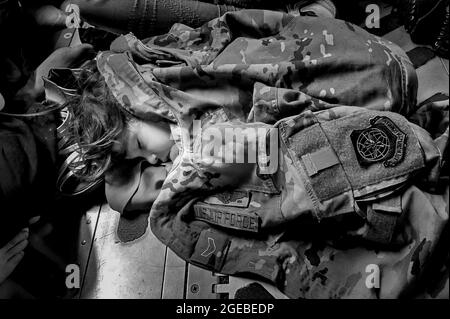 Un bambino afghano dorme sul pavimento di carico di un'aeronautica degli Stati Uniti C-17 Globemaster III, tenuto caldo dall'uniforme di Airman First Class Nicolas Baron, C-17 loadmaster, durante un volo di evacuazione da Kabul, Afghanistan, 18 agosto 2021. Operando una flotta di Air National Guard, Air Force Reserve e Active Duty C-17s, Air Mobility Command, a sostegno del Dipartimento della Difesa, ha spostato le forze in teatro per facilitare la partenza e il trasferimento sicuro dei cittadini statunitensi, dei beneficiari del visto speciale per l'immigrazione e delle popolazioni afghane vulnerabili dall'Afghanistan. (Foto: 1° Lt. Mark Lawson) Foto Stock