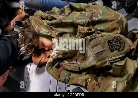 Un bambino afghano dorme sul pavimento di carico di un'aeronautica degli Stati Uniti C-17 Globemaster III, tenuto caldo dall'uniforme di Airman First Class Nicolas Baron, C-17 loadmaster, durante un volo di evacuazione da Kabul, Afghanistan, 18 agosto 2021. Operando una flotta di Air National Guard, Air Force Reserve e Active Duty C-17s, Air Mobility Command, a sostegno del Dipartimento della Difesa, ha spostato le forze in teatro per facilitare la partenza e il trasferimento sicuro dei cittadini statunitensi, dei beneficiari del visto speciale per l'immigrazione e delle popolazioni afghane vulnerabili dall'Afghanistan. (Foto: 1° Lt. Mark Lawson) Foto Stock