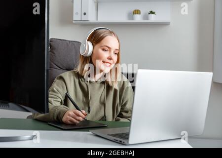 Giovane artista graphic designer donna che si avvale di una tavoletta grafica digitale di Stylus PEN che utilizza un monitor per PC portatile all'interno dell'ufficio. Freelance Foto Stock