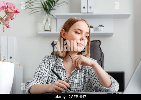 Giovane donna freelance grafico che lavora utilizzando grafica tablet e laptop in casa ufficio interni. Bionda caucasica fiduciosa focalizzata donna che fa Foto Stock