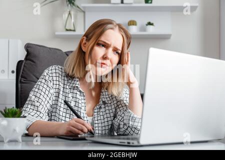 Insoddisfatto sconvolto donna stanca lavora con mal di testa in stress utilizzando grafica tablet laptop in ufficio interni. Freelance retoucher designer hanno Foto Stock