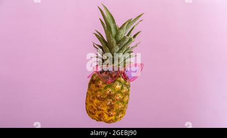 Ananas facce creative in occhiali da sole a colori su sfondo estivo di colore rosa. Tropicale frutta di ananas estate levitating in vetri rosa del sole. Estate Foto Stock