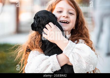 Bambina di capelli rossi abbracciando il suo nuovo amico, carino cucciolo nero Foto Stock