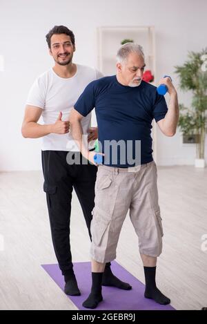 Giovane istruttore e vecchio che fa esercizi sportivi Foto Stock