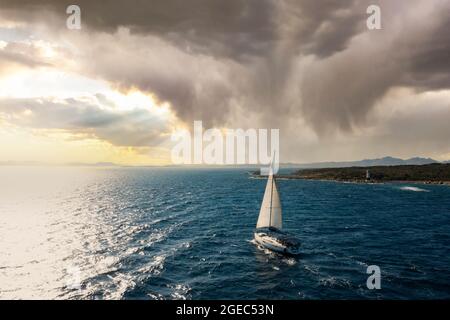 Vista dall'alto, splendida vista aerea di una barca a vela in barca a vela su un'acqua blu durante un bellissimo e suggestivo tramonto. Costa Smeralda, Sardegna, Italia. Foto Stock