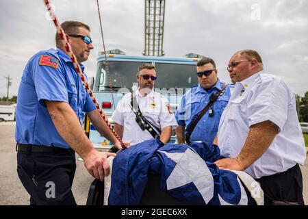 Bloomington, Stati Uniti. 18 agosto 2021. I vigili del fuoco aspettano per contribuire a sollevare una bandiera americana per la processione funeraria di caduto paramedico Brandon Staley morto da un attacco di cuore mentre funzionava come paramedico per il pronto soccorso della contea di Owen (Emergency Medical Services). Staley aveva appena risposto a un incidente stradale e si trovava in un'ambulanza con i sopravvissuti agli incidenti che li aiutavano durante il viaggio verso un ospedale quando egli stesso si ammalò. Credit: SOPA Images Limited/Alamy Live News Foto Stock