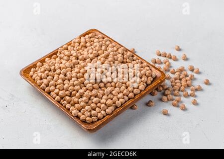 Ceci essiccati in un piatto quadrato di legno su sfondo grigio. Primo piano. Foto Stock