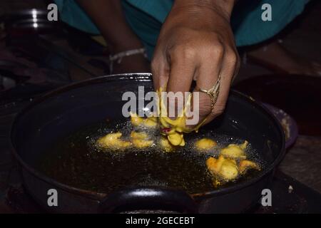 mani di una donna frittura di grammo di farina spuntini, bollente olio in padella con fondo scuro Foto Stock