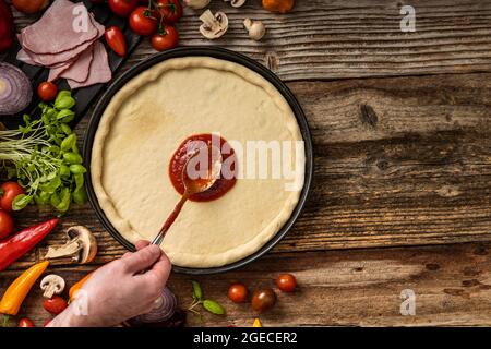 Pasta di pizza cruda e deliziosa con souce rosso sul tavolo di legno Foto Stock