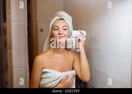 Scrubber ad ultrasuoni per la pulizia della pelle del viso. Ragazza in bagno si prende cura del suo viso Foto Stock