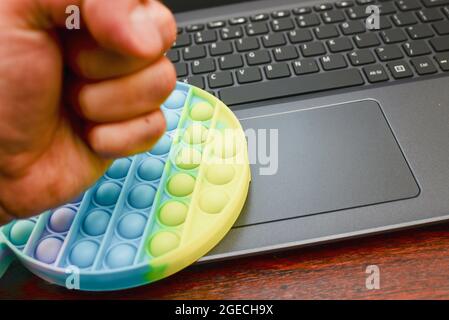 businessman mano nervoso pugno anti-stress giocattoli pop-it sulla tastiera. Il nuovo popolare giocattolo anti-stress in silicone colorato lo schioccano per eliminare lo stress. Foto Stock