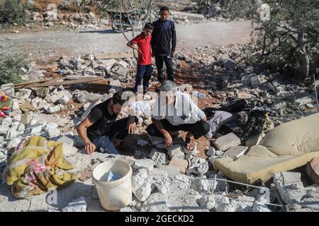 Balashun, Siria. 19 agosto 2021. La gente cerca i superstiti sotto le macerie di una casa dopo un missile che lo ha preso di mira nella città di Balashun nella regione di Jabal al-Zawiya (Monte Zawiya). Credit: ANAS Alkharboutli/dpa/Alamy Live News Foto Stock