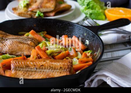 Filetto di salmone fritto in padella con cavolo e carote servito caldo in una padella in ghisa sul fondo del tavolo da cucina Foto Stock