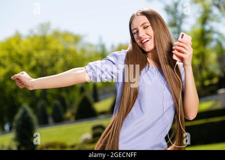 Foto di allegro ispirato signora danza vicino occhi tenere telefono ascoltare musica in auricolari indossare blusa fuori Foto Stock