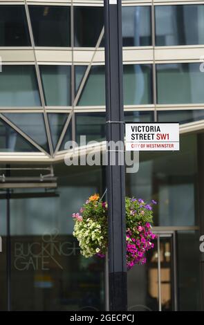 Londra, Inghilterra, Regno Unito. Cartello stradale: Victoria Street, City of Westminster, con fiori in cesti appesi Foto Stock