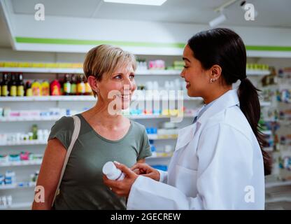 Madre di mezza età che ottiene assistente da intern femminile misto di razza che aiuta a prescrivere il farmaco Foto Stock