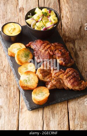 Autentica bistecca di maiale marinata Schwenkbraten con insalata di patate, senape e toast da vicino nella tavola di ardesia sul tavolo. Verticale Foto Stock