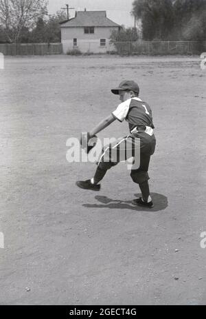 Anni '50, storico, all'esterno su una grande area polverosa di terreno aperto o sandlot, un giovane ragazzo americano nel suo kit di baseball e con caraffe guanto, giocando a baseball, Mid-West, USA. Foto Stock