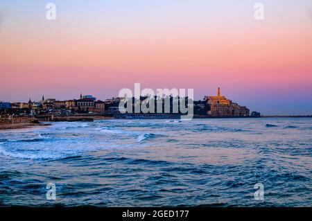 Israele, Jaffa come visto da nord a Alba. Il vecchio porto sulla destra e la torre campanaria della chiesa e monastero di San Pietro in centro Foto Stock
