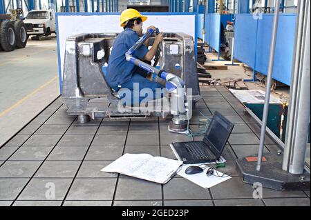 Un tecnico utilizza un'apparecchiatura di misurazione e un computer portatile in un impianto di fabbricazione di metalli. Foto Stock