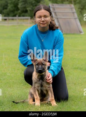 Una ragazza adolescente si pone insieme al suo cucciolo di Pastore tedesco. Addestramento del cane Foto Stock