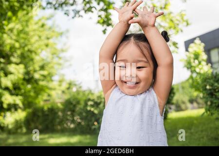 allegro bambino asiatico in piedi con le mani sollevate fuori Foto Stock