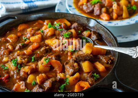 Stufato di manzo con carote e patate in una padella di ghisa sul tavolo da cucina Foto Stock