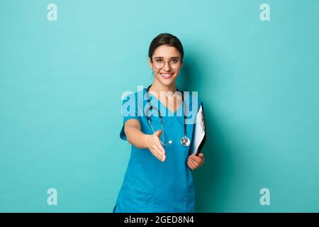 Concetto di coronavirus, pandemia e allontanamento sociale. Immagine di sicuro bella dottoressa, sorridente ed estensibile mano per stretta di mano, saluto Foto Stock