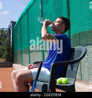Giovane professionista giocatore di tennis che beve acqua durante la pausa dopo il duro set Foto Stock
