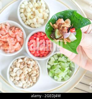 Mano ravvicinata con antipasto in foglia reale o Miang Kham, autentici spuntini thailandesi, gamberi salati secchi, zenzero, peperoncino, limone, arachidi tostate. Foto Stock