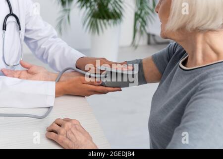 Vista tagliata del medico afroamericano che indossa tonometro su donna in ospedale Foto Stock