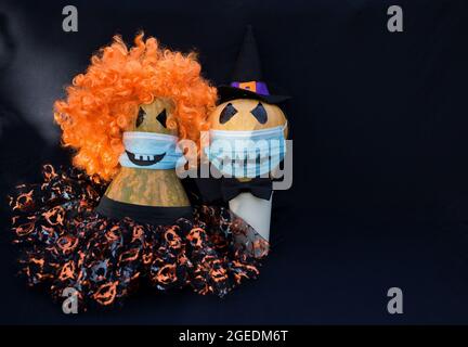 Festeggiando Halloween in una nuova realtà della pandemia COVID-19. Coppia di zucche innamorati indossare maschere mediche blu di protezione con orribile sorriso gettin Foto Stock