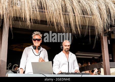 Disc jockey che suonano musica per i turisti al club party all'aperto sulla spiaggia - DJ che indossano le cuffie al Music Live Event - Live Event, musica e. Foto Stock