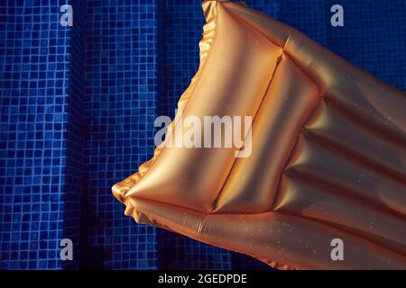 Materasso da nuoto dorato in piscina contro l'acqua blu al tramonto. Vacanza e vacanza concept foto. Spazio libero. Vista dall'alto. Foto Stock