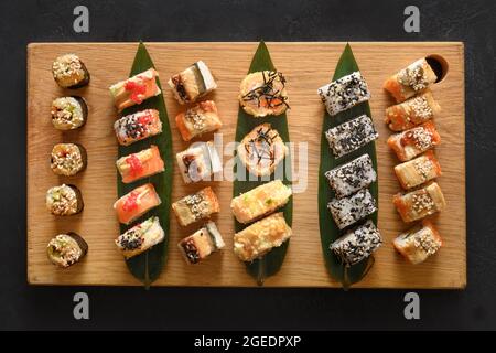 Set di sushi servito su tagliere di legno su sfondo nero. Vista dall'alto. Disposizione piatta. Foto Stock