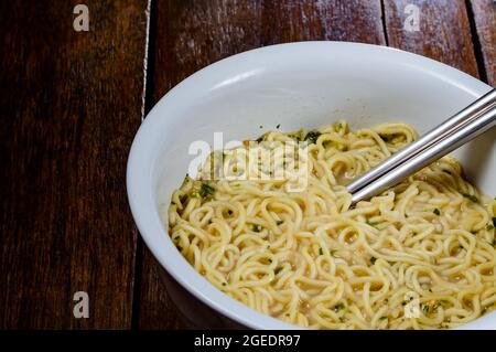 pronti a mangiare tagliatelle istantanee cotte in recipiente bianco e bastoncini di acciaio inossidabile su tavolo di legno scuro Foto Stock