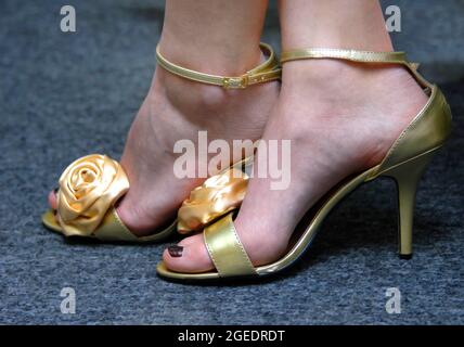 I piedi della donna sono elegantemente rivestiti in sandali con reggetta d'oro. Tacchi alti e rose dorate accentuano i piedi in forma. Foto Stock