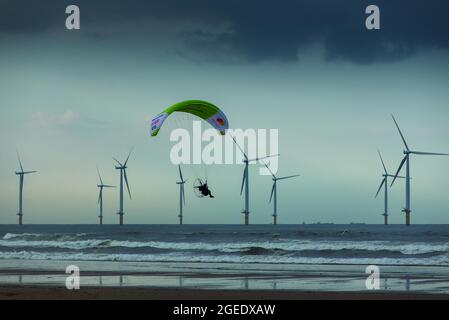 Sacha Dench il cigno umano che vola il suo parapendio elettrico lungo Coatham Beach con Teesside Windfarm oltre. Redcar, N Yorkshire, Inghilterra Foto Stock