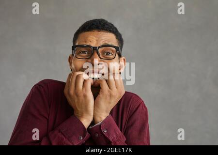 L'uomo afroamericano morde le dita ravvicinato il ritratto del viso girato su una parete grigia Foto Stock