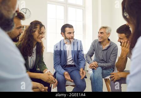 Giovane allenatore di affari o psicologo che ha una discussione con un gruppo felice di persone Foto Stock