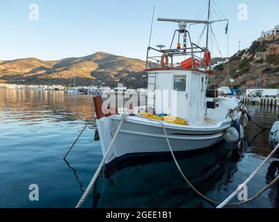 Isola di Sifnos, Platis Gialos, Cicladi Grecia. Tradizionale barca da pesca bianca ormeggiata al molo. Gli yacht di lusso sono ancorati alla marina dopo la crociera in inf Foto Stock