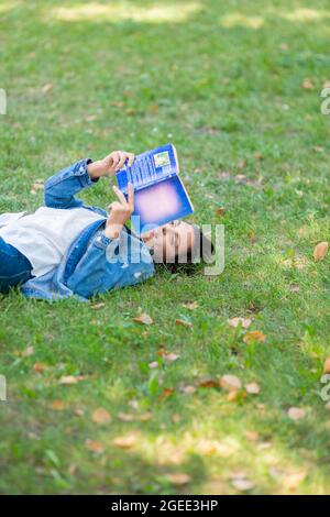 Foto verticale di una donna di mezza età che legge un libro nel parco. Lei si trova sul gras con un libro e prendere una pausa dal lavoro costante al compu Foto Stock