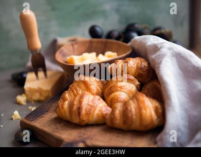 Croissant con formaggio e uva deliziosi per una gustosa colazione. Croissant francesi originali e gustosi con formaggio e sul tavolo in legno. Foto Stock