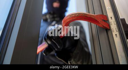 Scasso con palanchino. Burglar in balaclava che rompe una porta di vetro. Cameriera mascherata che entra in una casa per rubare durante il giorno. Foto Stock