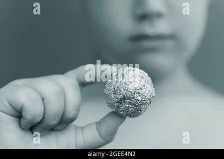 Giovane ragazzo che tiene un foglio di alluminio a forma di sfera Foto Stock