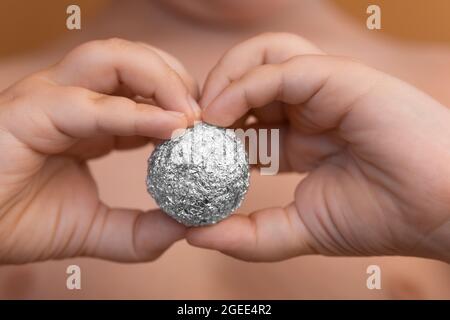 Giovane ragazzo che tiene un foglio di alluminio a forma di sfera Foto Stock