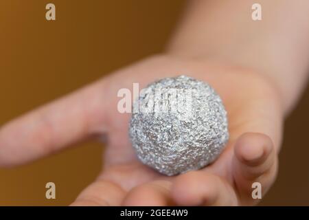 Giovane ragazzo che tiene un foglio di alluminio a forma di sfera Foto Stock