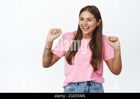 Immagine di danza moderna ragazza, ha tatuaggi a portata di mano e piercing, sorridendo e ridendo gioioso, in piedi su sfondo bianco Foto Stock